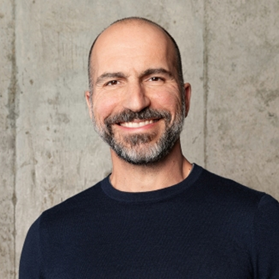 Dara Khosrowshahi, a man with a trimmed beard and mustache, wearing a dark t-shirt, smiling gently in front of a plain background.