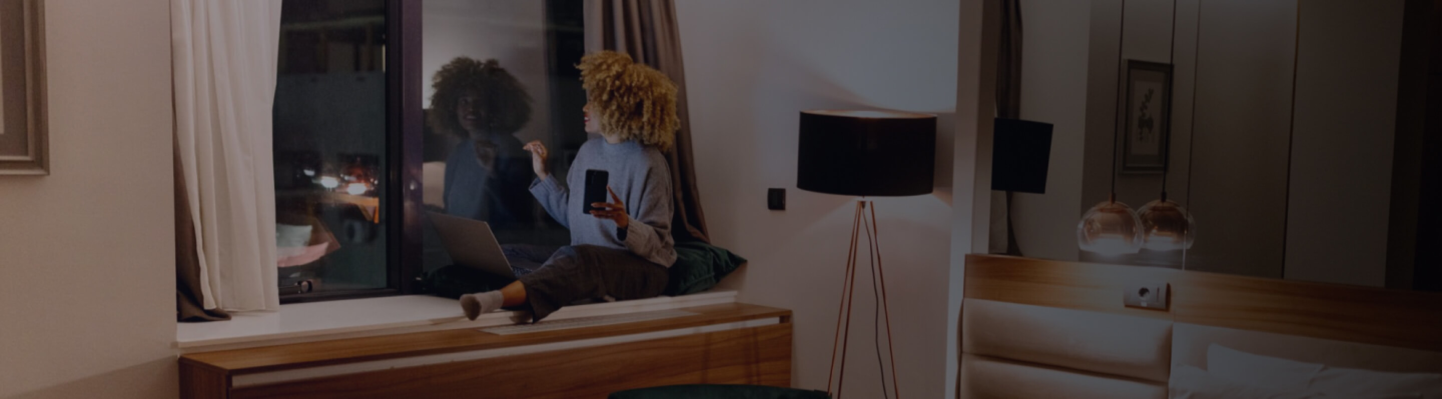 A woman using her laptop sitting against a window on a bench 
