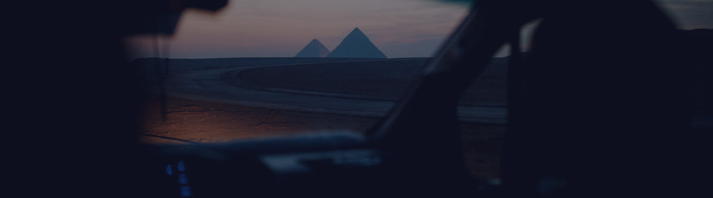 Vista das pirâmides ao pôr do sol vista de dentro de um veículo, com o painel em silhueta emoldurando a cena.