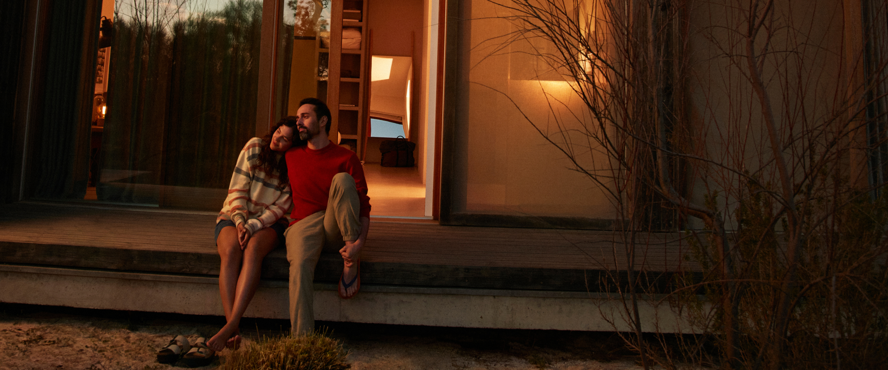 A couple sits together on the porch of a cozy cabin during the evening.