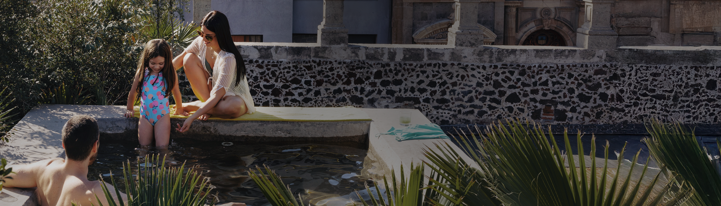 A family sits on a courtyard pool, dipping their feet in the water together.