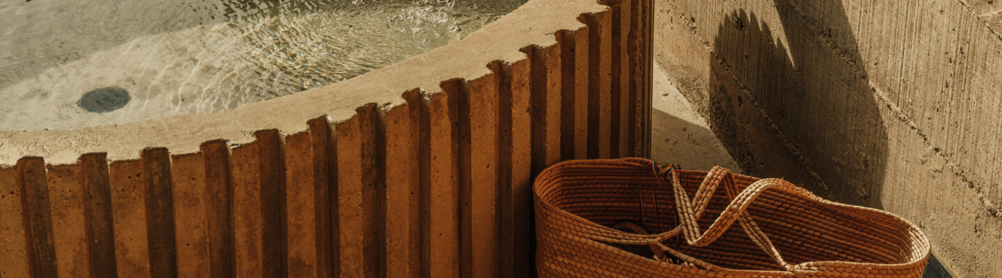 A straw totebag sits next to a water feature.