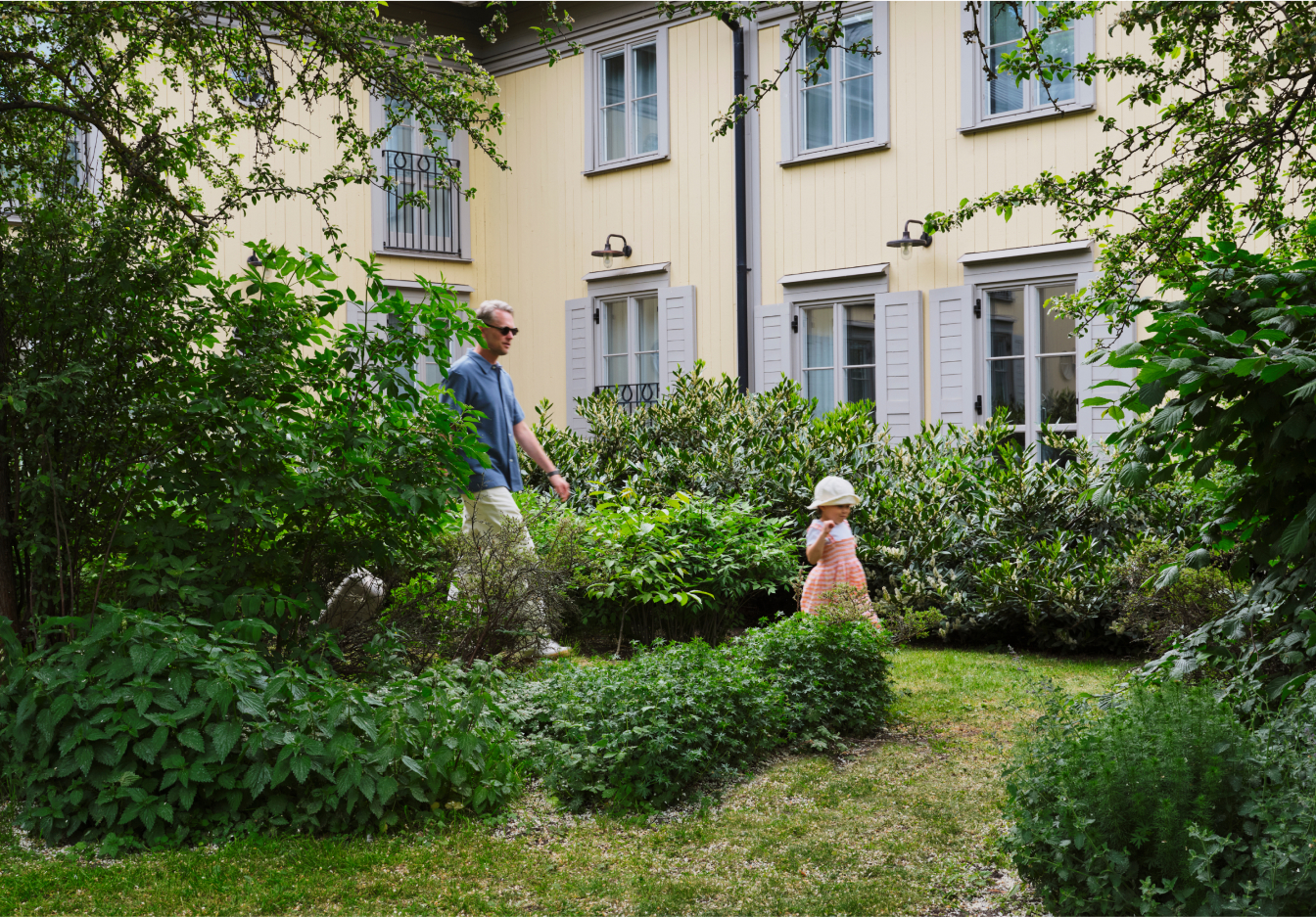 Photograph of a man walking behind a female child running through a hotel courtyard filled with grass and plants.