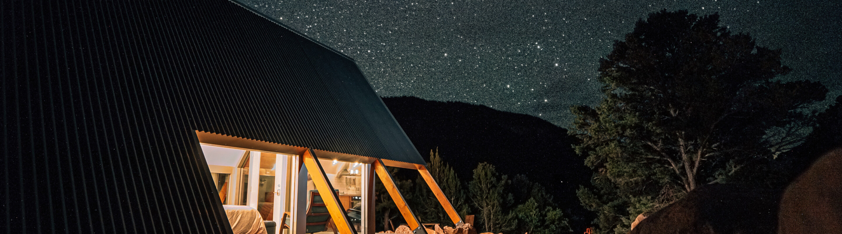 Modern A-frame cabin illuminated at night under a starry sky and surrounded by trees