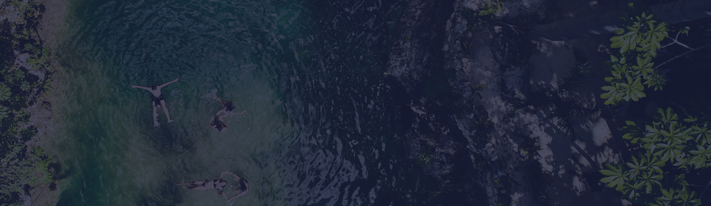 A birds eye view of a small group of friends floating in their swimwear in the green clear waters of a river in a tropical rainforest.