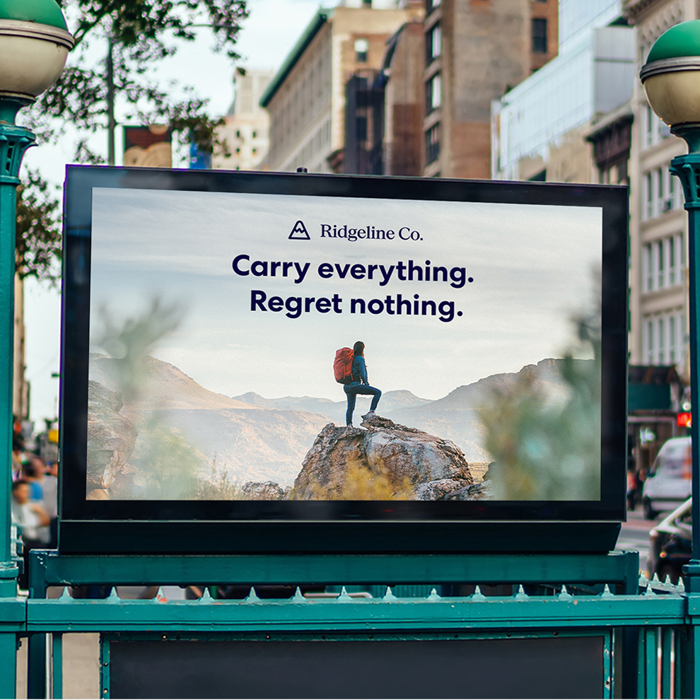 Outdoor billboard in a city streetscape displaying a Ridgeline Co. hiking ad with the headline “Carry everything. Regret nothing.”