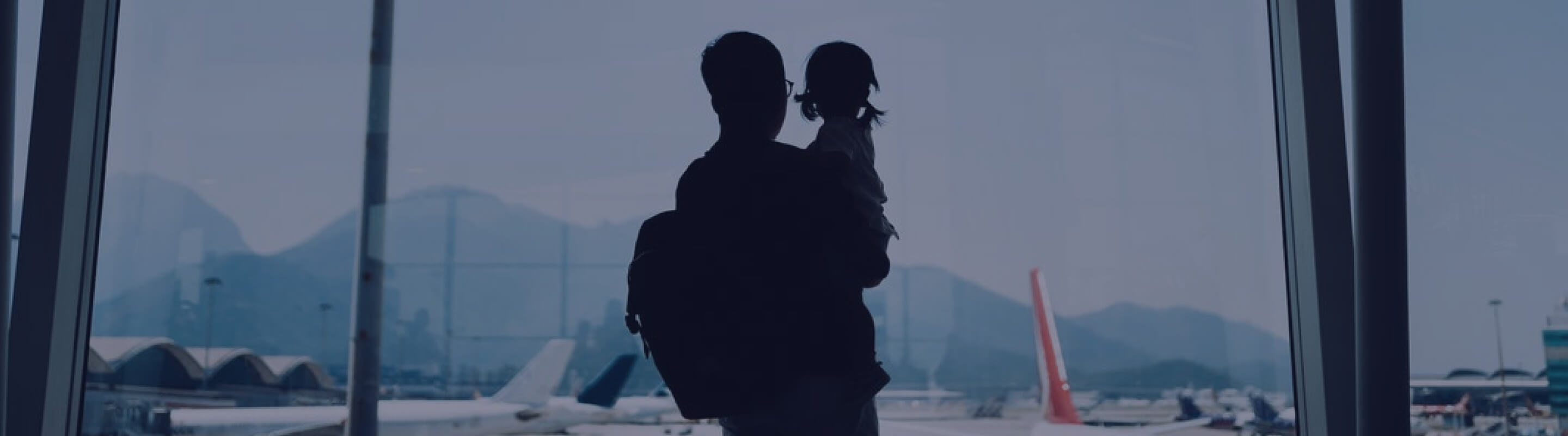 A man holds a child as they look out an airport window 