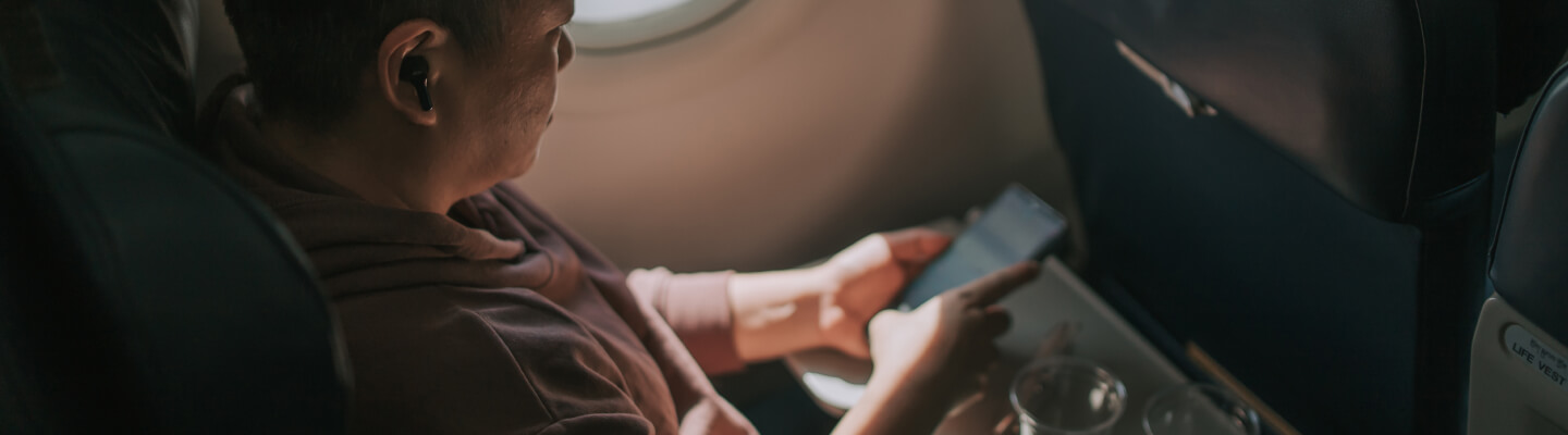 A man looks at his cell phone while sitting in an airplane seat.