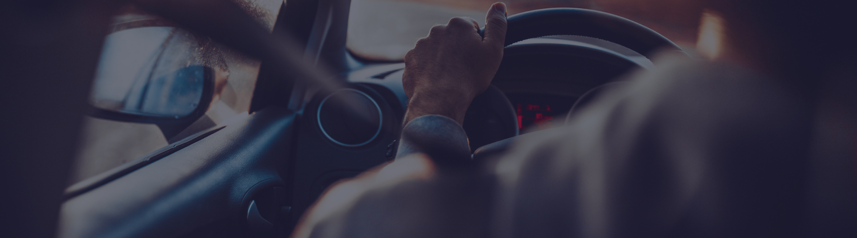 A closeup shot of hands on the steering wheel of a car.