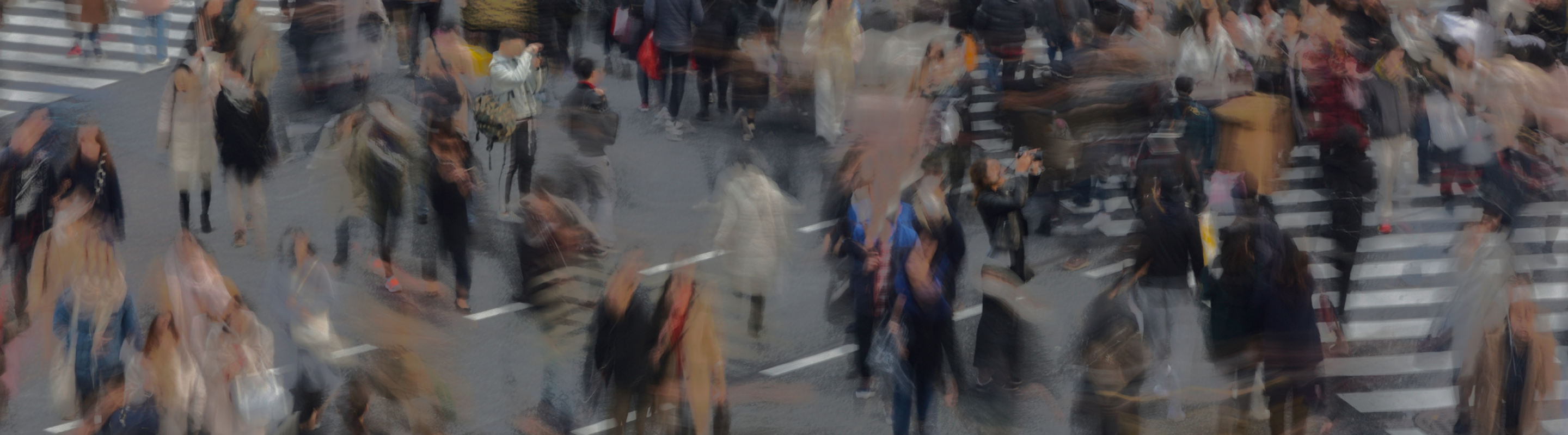 Blurred photo of a busy city crosswalk filled with people walking in multiple directions, creating a sense of movement.