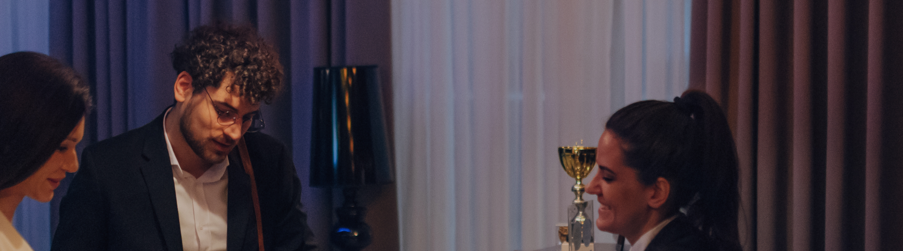 Two hotel guests at the front desk, checking in with a reception staff member in a warmly-lit lobby