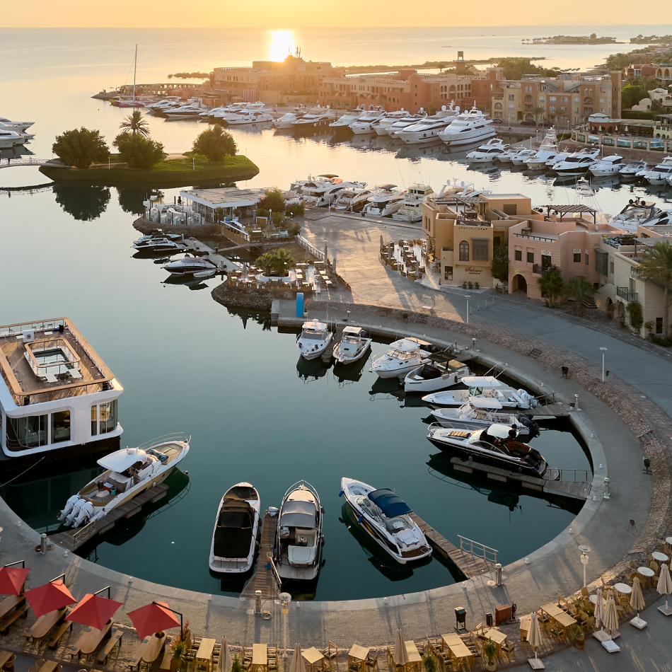 Elevated view of a harbor filled with boats, surrounded by waterfront buildings under a sunset sky.