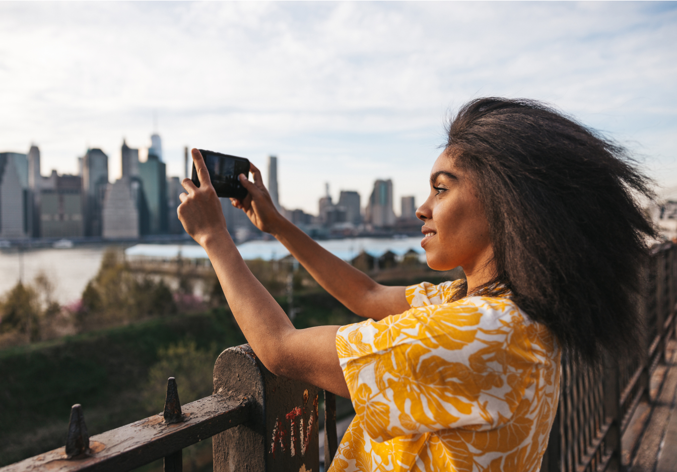 A woman wearing a short-sleeve shirt taking a picture of a city with her phone.